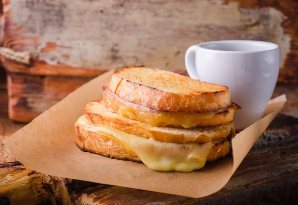 Сэндвич с сыром на бумаге на деревянной доске. Селективный фокус. — стоковое фото
