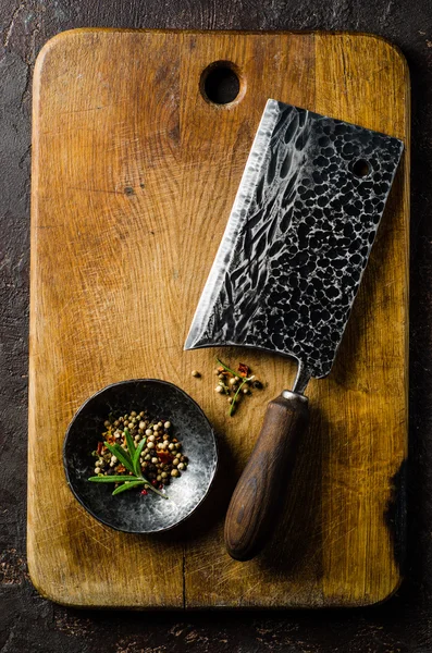 Chopping board block and Meat cleaver large chefs knife and bowl with spice on dark background. Vertical top view