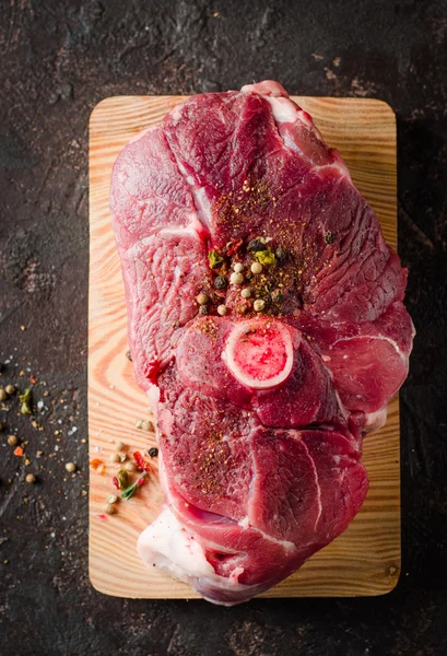 Carne crua de carneiro com especiarias na tábua de corte e fundo escuro. Foco seletivo. Vista superior — Fotografia de Stock