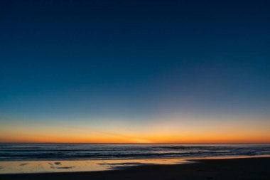 Sahildeki ıslak kumda ve karanlık ufuk çizgisinde kan kırmızı günbatımının yansıması.