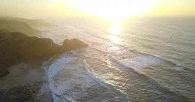 Yaklaşan dalgalarla bir plajın havadan görünüşü, gün batımında beyaz sprey.