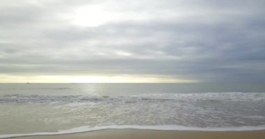 Yaklaşan dalgalarla bir plajın havadan görünüşü, gün batımında beyaz sprey.