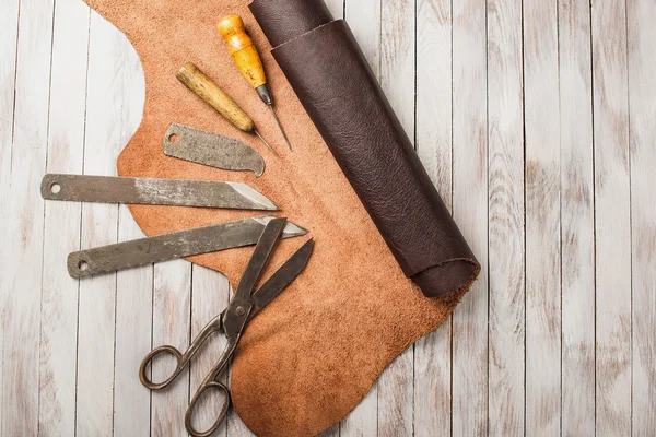 A secretária do Leathersmith. Pedaços de ferramentas de trabalho de couro e couro em uma mesa de trabalho . — Fotografia de Stock