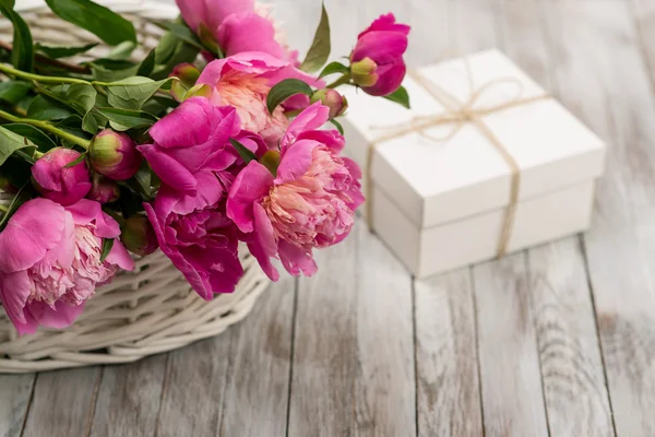 Красиві квіти півонії в кошику з подарунковою коробкою на світлому дерев'яному фоні . — стокове фото
