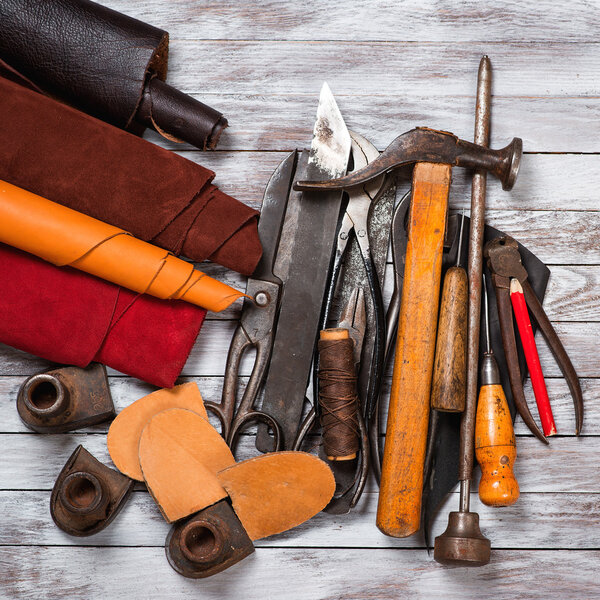 Set of leather in rolls, craft tools on white wooden background. Workplace for shoemaker. Working handmade tools on a work table.