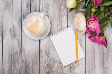 Defter bir kalem kahve ve peonies çiçek ahşap zemin üzerine yanındaki ile. Üstten Görünüm.