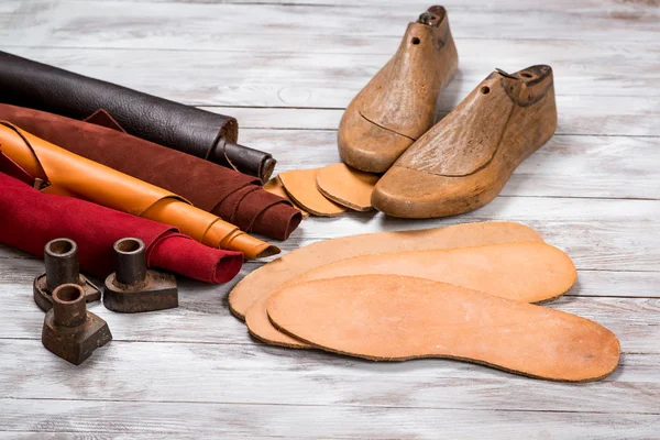 Set van leer met broodjes, ambachtelijke tools op witte houten achtergrond. Werkplaats voor de schoenmaker. Handgemaakte tools werken op een werktafel. — Stockfoto