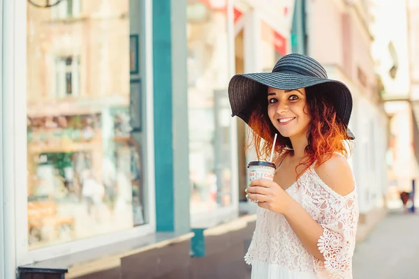 Chica bonita con el pelo rojo en un sombrero negro está bebiendo llevar c — Foto de Stock