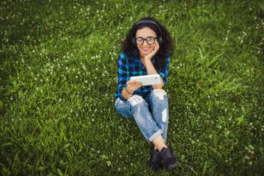 Tablet pc ve müzik açık havada için dinlerken kulaklık kullanarak mutlu güzel kız.