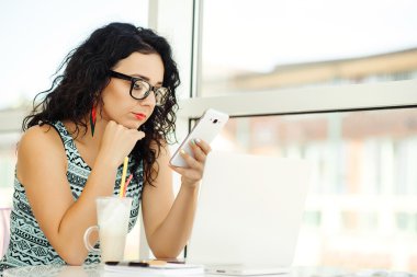 Dizüstü bilgisayar kullanarak ve cep telefonu üzerinde konuşurken güzel genç kadın.