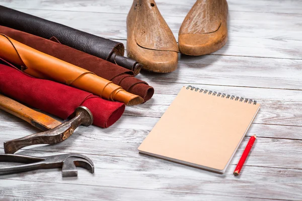 Brightly colored leather in rolls, working tools, shoe lasts, notebook with pencil on white background. Leather craft.