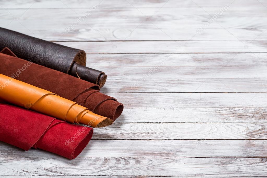 Brightly colored leather in rolls on white wooden background. Leather craft. Copy space.