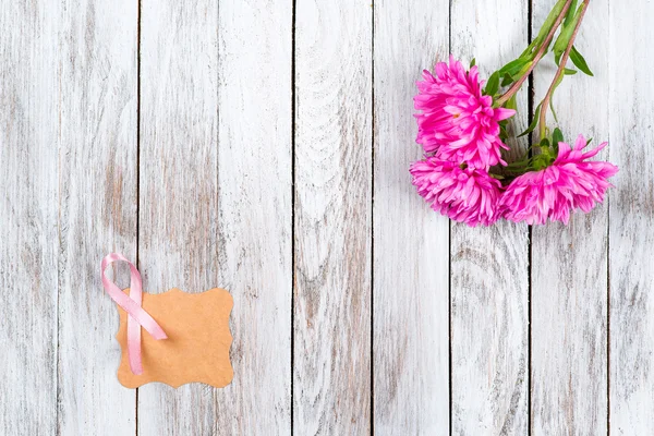Pink breast cancer ribbon and pink flowers on wooden background.