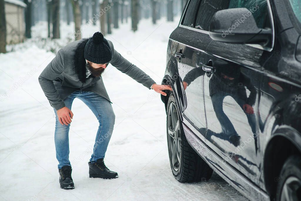 Man checking car tyre in winter. Businessman has problems with the wheels of the car. Winter snowy weather. Driving a car in winter.