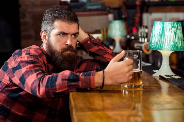 Sad man drinking beer at pub. Single bearded man at the bar counter. Alcohol addiction. Bearded man holds glass of beer.