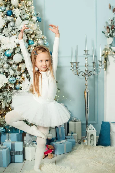 Little girl in ballerina costume dancing near christmas tree. Merry Christmas and Happy Holidays. Celebrating Xmas at home. Luxury decorations and christmas tree. Lovely girl enjoying christmas party
