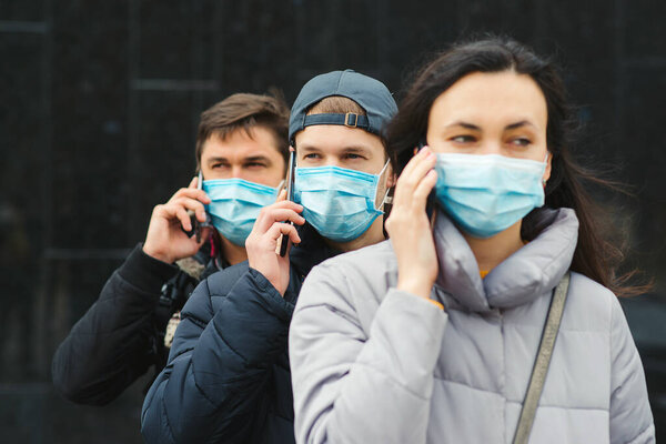 Group of young volunteers wearing face masks with mobile phones. Volunteers are ready to help. Call to volunteers. The concept of mutual assistance and support. World coronavirus pandemic.