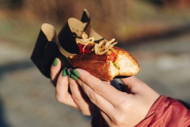Taze sosisli sandviç ve ızgara sosis tutan bir kadın. Sandviç kağıdında servis edilir, yakın çekim. Sokak yemeği, fast food..