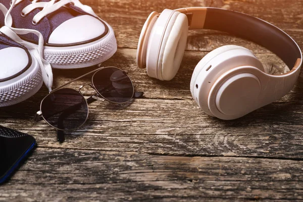 Headphones and sneakers on rustic background. Set of trendy men accessories. Fashion sneakers, sunglasses and modern wireless headphones. Male fashion. Copy space. Hipster urban style