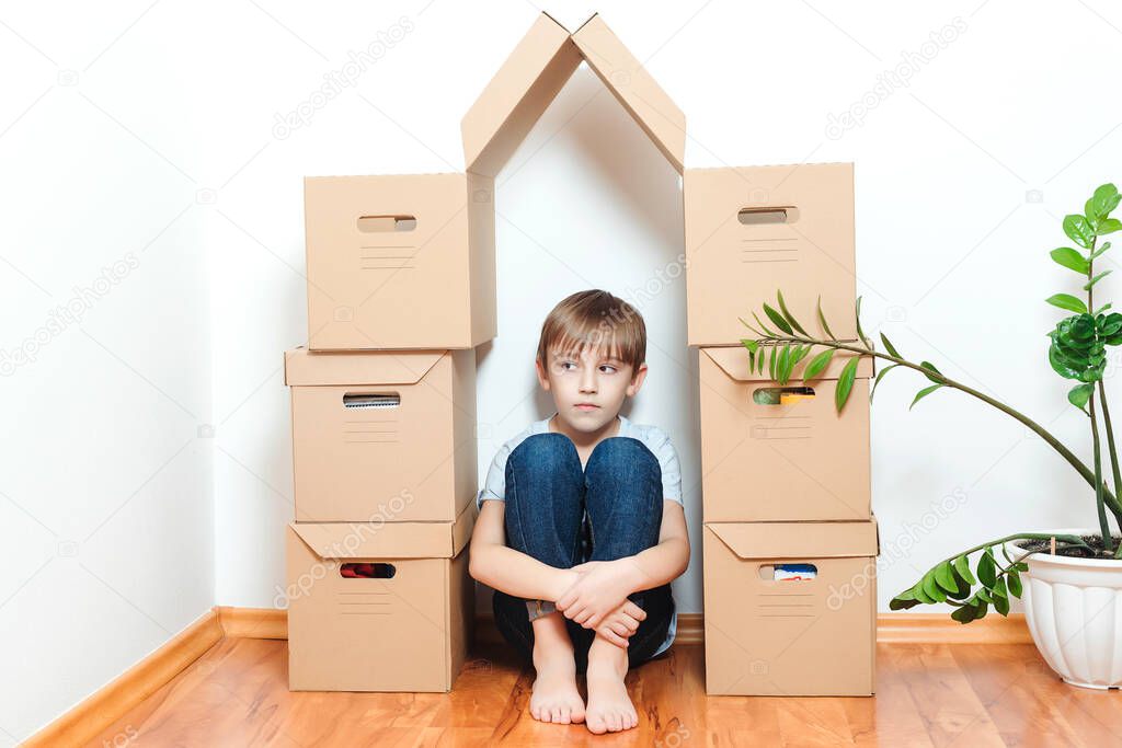 Sad child hiding in house making from boxes. Mortgage, people, housing, moving and real estate. Child dreaming about new home. Adoption concept.