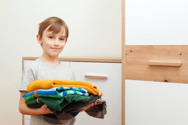 Çocuk dolabı düzene sokuyor. Renkli giysiler yığını. Gardıropta kıyafet düzenleyen bir çocuk. Dolapta sipariş verin. Çocuk kıyafetleri olan gardırop..
