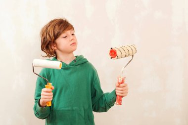 Çocuk duvarı silindirle boyuyor. Çocuk resim yapmak için fırça tutuyor. Küçük yardımcı. Küçük çocuk odasını yenilerken eğleniyor..