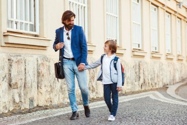 Okuldaki ilk günüm. Babamın birinci sınıfta bir oğlu var. Babası ve çocuğu sokakta el ele tutuşuyorlar. Okula geri dönüyorsun. Modaya uygun baba ve oğul resmi takım elbise giyiyor..