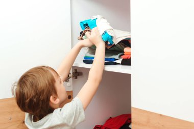 Çocuk dolabı düzene sokuyor. Gardıropta kıyafet düzenleyen bir çocuk. Dolapta sipariş verin. Çocuk giysi yığınını rafa koyuyor..