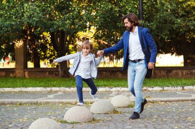 Mutlu çocuk ve baba yürüyüş yaparken eğleniyorlar. Yakışıklı bir baba ve şık takımlar giyen bir çocuk. Aile, moda ve yaşam tarzı. Oğlu şehir caddesinde yürüyen şık bir baba..