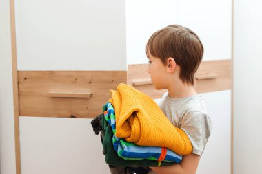 Çocuk dolabı düzene sokuyor. Renkli giysiler yığını. Gardıropta kıyafet düzenleyen bir çocuk. Dolapta sipariş verin. Çocuk kıyafetleri olan gardırop..