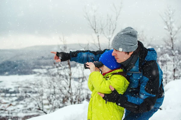 Happy dad and son at winter forest. Kid looking to monocular. Family winter holidays. Father and kid having fun together on nature. Father and son hiking in winter mountains.