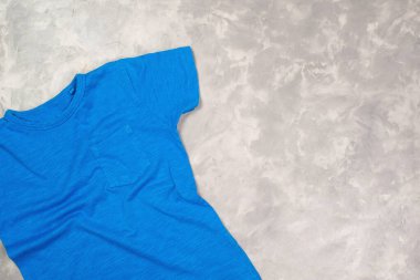 Fotokopi alanı olan mavi renkli tişört. Tişört modeli, düz yatış. Modern beton arkaplan.
