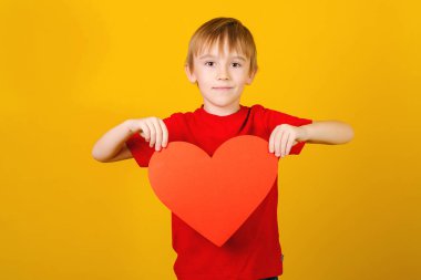 Kırmızı kalbi olan bir çocuk. Aşk kavramı, hayır kurumu ve sosyal bağış. Kırmızı kağıt kalpli şirin bir çocuk..