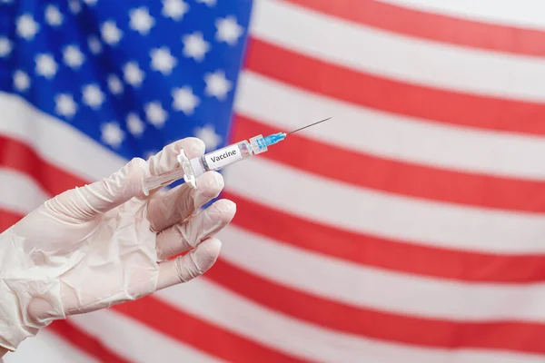 Doctor\'s hand holding syringe with vaccine over United States of America flag background. USA Vaccination. COVID-19 vaccine concept. Covid-19 vaccination, flu prevention, immunization concept.