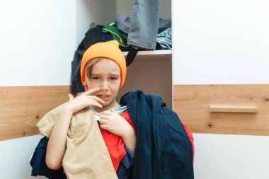 Kirli çamaşır yığını tutan çocuk. Dağınık giysi dolabı. Dağınık çocuk odası. Ev işleri ev işleri. Gardıropta karışıklık. Çocuk odasında bir sürü dağınık kıyafet var..