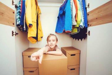 Yeni modern gardıropta oturan sevimli çocuk. Çocuk dolabında sipariş verin. Kutuları açmaya yardım eden mutlu çocuk. Aile yeni bir daireye taşınır..