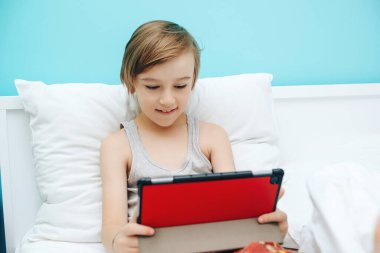 Yatmadan önce dijital alet kullanan sevimli bir çocuk. Çocuk video izler ve tablette oyunlar oynar. Çocukların internete ve cihazlara olan bağımlılığı.