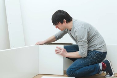 Adam evde yeni mobilya montajı yapıyor. Mobilyaları kendin monte et. Genç işçi bir kitaplık topluyor. Mobilya teması. Müteahhit modern apartmanda yeni mobilya montajı yapıyor..