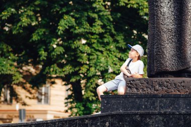 Şehirde dolaşan şirin, şık bir çocuk. Moda kıyafetleri ve bel çantası giyen mutlu bir çocuk. Yaz modası. Yakışıklı çocuk yaz tatilinin tadını çıkarıyor. Mutlu çocukluk.