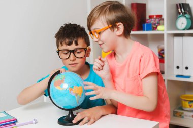 Okul çocukları dünyayı inceliyor. Eğitim ve coğrafya. Okula dönelim. Gülümseyen öğrenciler küreye bakıyor. Coğrafya okuyan zeki çocuklar. Çocuklar birlikte ödev yapıyorlar..