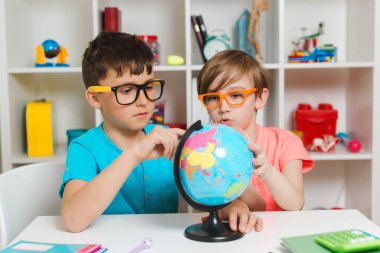 Okul çocukları dünyayı inceliyor. Eğitim ve coğrafya. Okula dönelim. Gülümseyen öğrenciler küreye bakıyor. Coğrafya okuyan zeki çocuklar. Çocuklar birlikte ödev yapıyorlar..