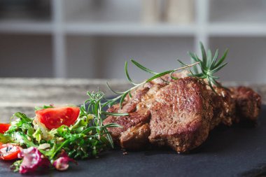 Siyah taş levhada ızgara biftek. Lezzetli ızgara biftek ve domatesli salata. Ana yemek sığır eti. Biftek ve salatalı akşam yemeği. Tahtada büyük para var..