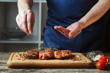 Şefin elleri biftek pişiriyor. Şef çiğ ete tuz ve biber ekliyor. Adam mutfakta biftek pişiriyor. Tahtada biftek pişiriyorum..
