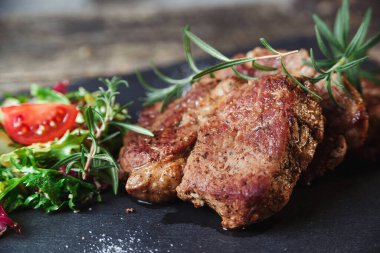 Siyah taş levhada ızgara biftek. Lezzetli ızgara biftek ve domatesli salata. Ana yemek sığır eti. Biftek ve salatalı akşam yemeği. Tahtada büyük para var..
