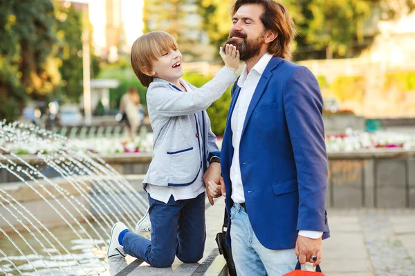 Happy dad and son fooling on a walk. Businessman with kid having fun together outdoors. Happy father's day. Bearded man and child enjoying near street fountain.