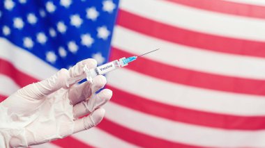 Corona virüsü aşısı ve şırınga enjeksiyonu. Amerika Birleşik Devletleri Aşısı. Arka planda Amerikan bayrağı. Ellerinde Coronavirus aşısı olan bir doktorun elleri..