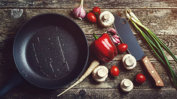 Ahşap arka planda mutfak aletleri ve baharatlar, üst manzara. Koyu ahşap masada yemek arkaplanı. Siyah tavayla yemek pişirmek için gerekli malzemeler. Yemek pişirmek için çeşitli ürünler.