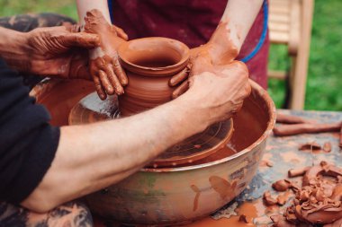 Potter çocuklara çanak çömlek üzerinde seramik demlik yapmayı öğretiyor. Dışarıda çömlek atölyesi var. Çömlekçiler ve çocuk elleri. Aile çömlek çarkında çalışıyor. Baba ve çocuk birlikte seramik demlik yapıyorlar..