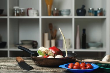 Mutfak tezgahında tava ve vejetaryen mutfak malzemeleri var. Mutfak arka planında bulanık aletler. Tava ve sebzeli yemek pişirme geçmişi.