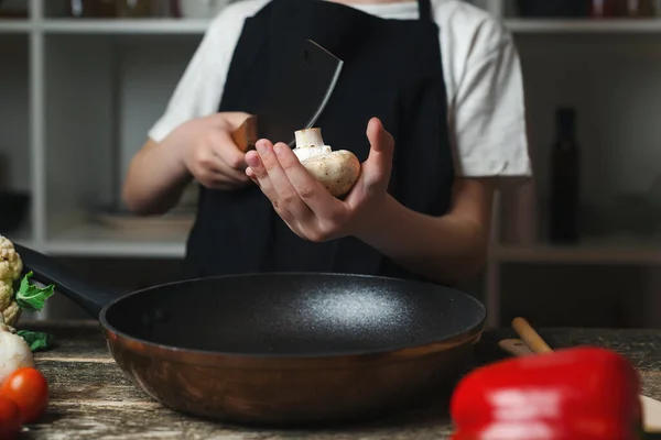 厨师切新鲜蘑菇做饭 厨师在做饭 儿童厨师在厨房做饭 男孩穿着厨师围裙和帽子 男孩在木板上切蔬菜 — 图库照片